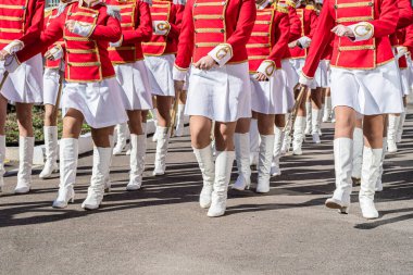 Large group of young girls in red and white ceremonial suits march in formation on a city street. Festive procession of drummers. Front view.