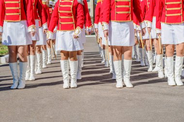 Large group of young girls in red and white ceremonial suits march in formation on a city street. Festive procession of drummers. Front view.