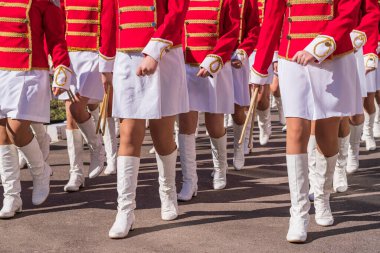 Large group of young girls in red and white ceremonial suits march in formation on a city street. Festive procession of drummers. Front view.