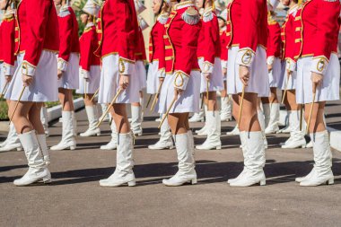 Large group of young girls in red and white ceremonial suits march in formation on city street. Festive procession of drummers. Side view.