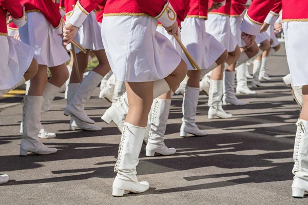 Large group of young girls in red and white ceremonial suits march in formation on city street. Festive procession of drummers. Side view.