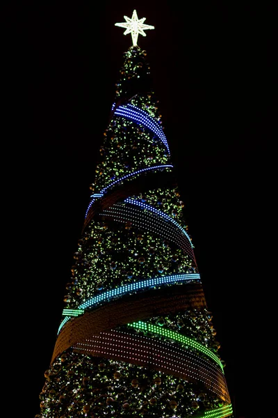 夜空の黒い背景に明るい光とガーランドで飾られた美しい背の高いクリスマスツリー — ストック写真