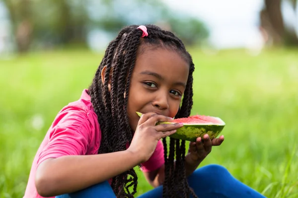 Retrato ao ar livre de uma linda jovem menina negra comendo água — Fotografia de Stock
