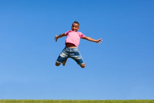 Outdoor portrait of a cute teenage black boy jumping over a blue — Stock Photo, Image