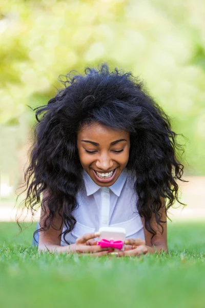 Adolescente menina negra usando um telefone, deitado na grama - p Africano — Fotografia de Stock