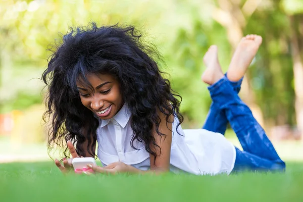 Teenage zwarte meid met behulp van een telefoon, liggend op het gras - Afrikaanse p — Stockfoto