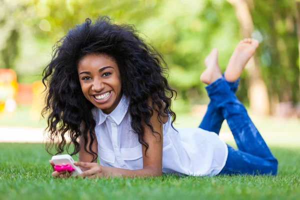 Teenage black girl using a phone, lying on the grass - African p — Stock Photo, Image