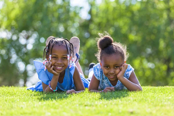 Outdoor portrait of a cute young black sisters  lying down on th — Stock Photo, Image