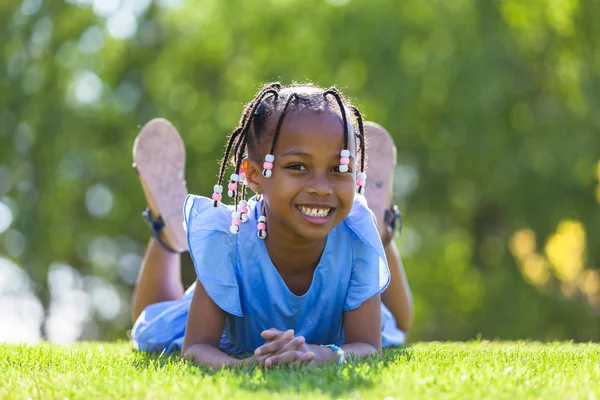 Außenporträt eines netten jungen schwarzen Mädchens, das sich auf den Boden legt — Stockfoto