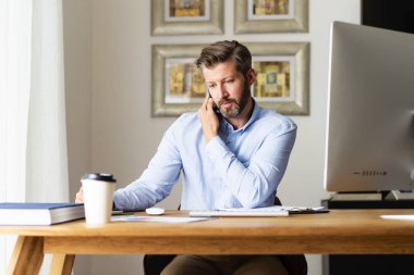 Kendine güvenen iş adamı masasında oturup çalışırken cep telefonunu kullanıyor ve biriyle konuşuyor. Merkez Ofis.