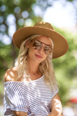Açık havada dinlenirken güneş gözlüğü ve şapka takan çekici sarı saçlı kızın yakın plan portresi..