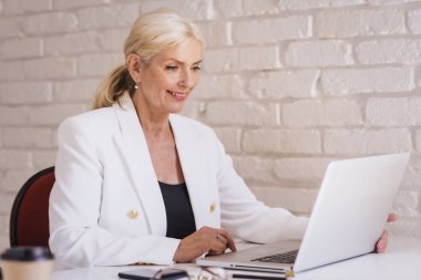 İnternette çalışırken dizüstü bilgisayar kullanarak gülümseyen kıdemli iş kadını. Merkez Ofis. 