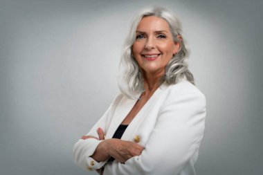 Gri arka planda dikilirken zarif kıyafetler giyen gri saçlı yaşlı bir kadının stüdyo fotoğrafı. Boşluğu kopyala.