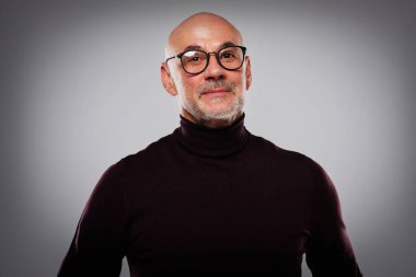 Gözlük ve balıkçı yaka kazak giyen gülümseyen orta yaşlı bir adamın stüdyo portresi izole gri arka planda kolları katlanmış dikilirken. Boşluğu kopyala. 