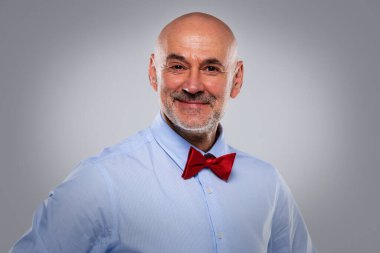 İzole edilmiş gri arka planda dikilirken papyon ve gömlek takan orta yaşlı mutlu bir adamın vesikalığı. Boşluğu kopyala.