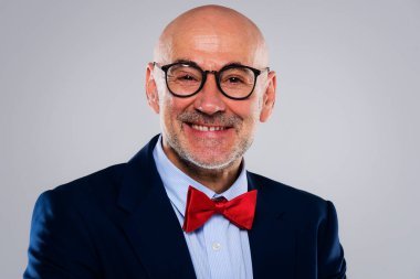 Gri arka planda dikilirken takım elbise ve papyon takan gülümseyen işadamının vesikalığı. Boşluğu kopyala.