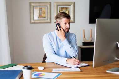 İşadamı bilgisayarının arkasında oturuyor ve bir telefon görüşmesi yapıyor. Merkez Ofis.