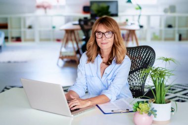 Ofiste oturup dizüstü bilgisayarla çalışan kendine güvenen bir iş kadını..