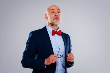 Gri arka planda dikilirken, şaşırmış yüzlü, takım elbiseli ve papyonlu bir iş adamı görüntüsü. Boşluğu kopyala.