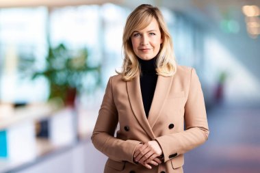 Kurul odasında dikilirken balıkçı yaka kazak ve ceket giyen güzel sarı saçlı iş kadını..