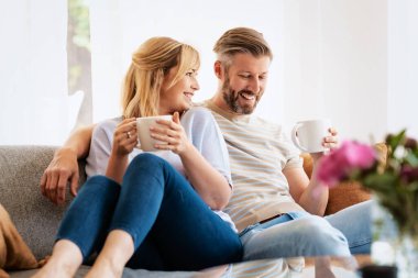 Candid shot of happy couple relaxing on the couch at home while drinking tea. 