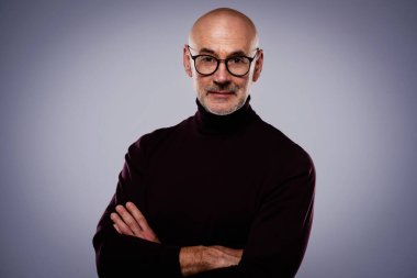 Gri arka planda dikilirken sıradan kıyafetler giyen orta yaşlı yakışıklı bir adamın stüdyo portresi. 