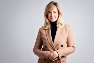 Gri arka planda dikilirken balıkçı yaka kazak ve ceket giyen çekici sarı saçlı kadının stüdyo portresi.. 