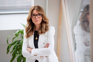 Pencerenin yanında duran kendinden emin orta yaşlı iş kadını portresi.