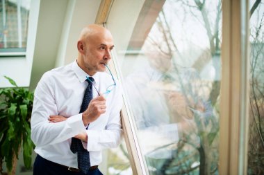 Tişört ve kravat takmış gülümseyen bir işadamının pencerenin önünde dikilirken düşünceli bakışları..