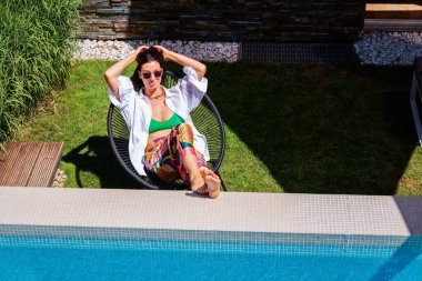 Havuz kenarında dinlenirken mayo ve plaj kıyafeti giyen çekici bir kadının fotoğrafı.. 