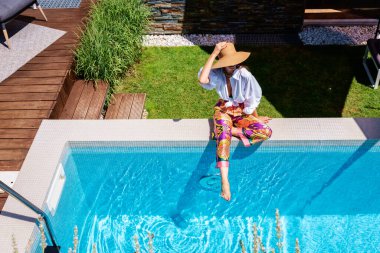 From above shot of unrecognizable woman wearing straw hat and white shirt while relaxing at the swimming pool. Shot from above. 