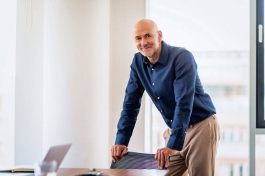 Portrait of successful middle aged businessman wearing shirt while standing at a modern office.