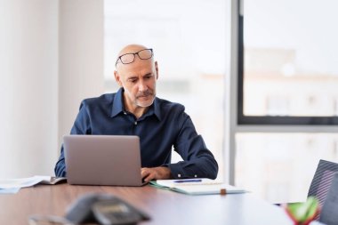 Shot of a thinking businessman using a laptop while sitting at office desk and working. 