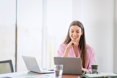 Smiling businesswoman using laptops while sitting at desk and working at a modern office.
