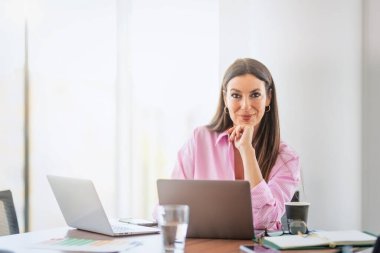 Smiling businesswoman using laptops while sitting at desk and working at a modern office.