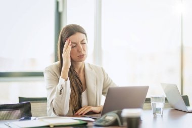 Cropped shot of an attractive businesswoman sitting alone in her office and suffering from a headache.