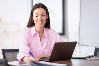 Smiling businesswoman using a laptop while sitting at desk and working at a modern office.