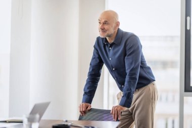 Middle aged businessman looking thoughtfully while sitting at office desk in a modern office.