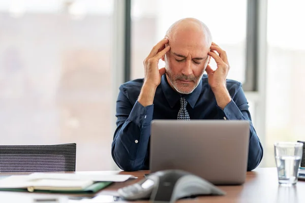 Shot of exhausted businessman with hands on his forehead sitting in the office. Professional man having pain in his head.