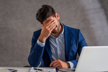 Shot of stressed businessman sitting at desk in office with laptop. Professional man suffering from migraine. 