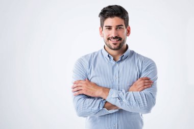 Studio portait of handsome man standing with arms crossed. Copy space. Male is wearing blue shirt against white background. He is smiling.