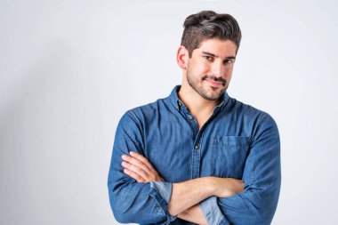 Studio portait of handsome man standing with arms crossed. Copy space. Male is wearing denim shirt against white background. He is smiling.