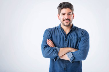 Studio portait of handsome man standing with arms crossed. Copy space. Male is wearing denim shirt against white background. He is smiling.