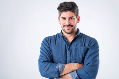 Studio portait of handsome standing with arms crossed. Copy space. Male is wearing denim shirt against white background. He is smiling.