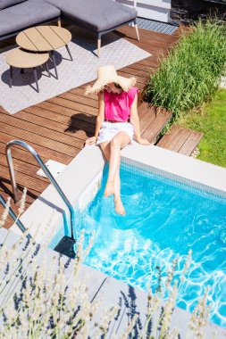 High angle shot of a woman wearing straw hat and pink t-shirt while relaxing by the poolside. 