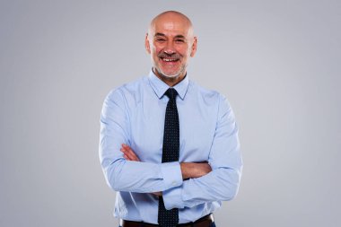 Portrait of smiling caucasian mature businessman. Confident male professional with arms crossed is wearing shirt and tie. He is against grey background.