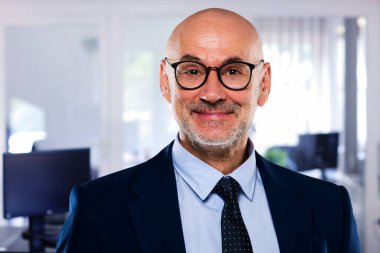 Close-up portrait of smiling caucasian mature businessman. Confident male professional is wearing blazer and eyewear.. He is standing at the office.
