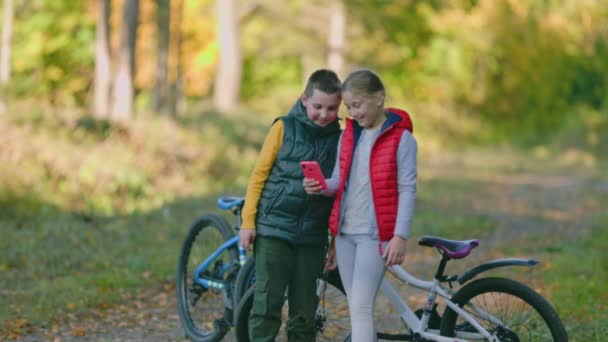 Barn Står Nära Cyklar Och Titta Telefonen — Stockvideo