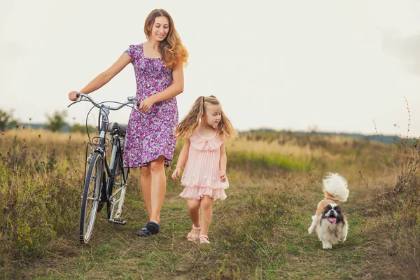 Mother and daughter walking with a bicycle and a dog — Stock Photo, Image