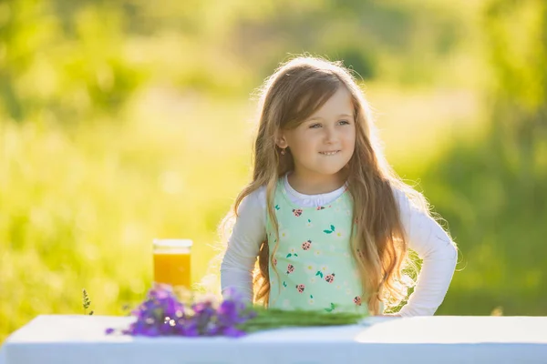 Wesoła dziewczyna siedzi przy stole, na którym stoi sok pomarańczowy — Zdjęcie stockowe